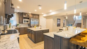 A modern kitchen with dark wood cabinets, a central island, and stainless steel appliances. - 6 Bed 5 Bath Beach Home with Elevator, Pool & Decks Steps from the Beach (Brigantine)