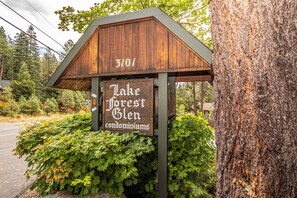 A wooden sign with 'Lake Forest Glen condominiums' written on it, mounted on a post with a green roof.