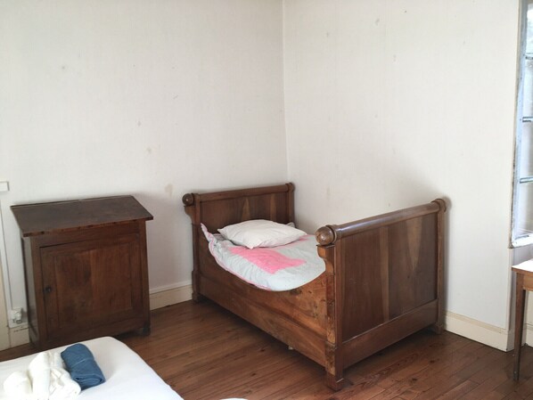 A small, single-bed room with a wooden headboard, a wooden nightstand, and a window with blinds.