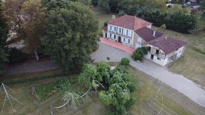 Eine Vogelperspektive zeigt ein zweistöckiges Haus mit rotem Ziegeldach, umgeben von Bäumen und einem gepflegten Rasen.