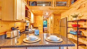 Interior de una cabaña de madera con área de cocina que incluye encimeras de granito, una tostadora y un cartel de bienvenida.