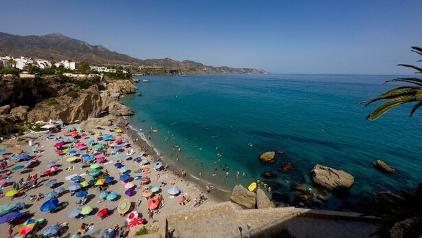Una playa con numerosos paraguas de colores y gente disfrutando del agua.