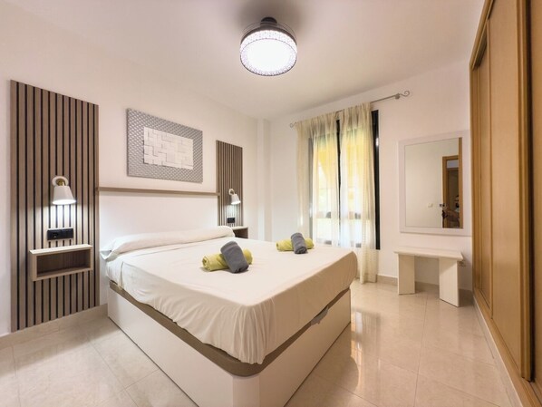 A modern hotel room with a large bed, bedside lamps, a bedside table, a mirror, and a window with curtains.