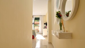 Un pasillo con suelo de baldosas blancas, una recepción con un florero y vistas a un comedor con mesa y sillas.