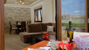 Ein modernes Wohnzimmer mit Steinwand, einem braunen Sofa, einer Essecke mit Stühlen und einem Tisch mit einer Weinflasche, Gläsern und Wassermelone.