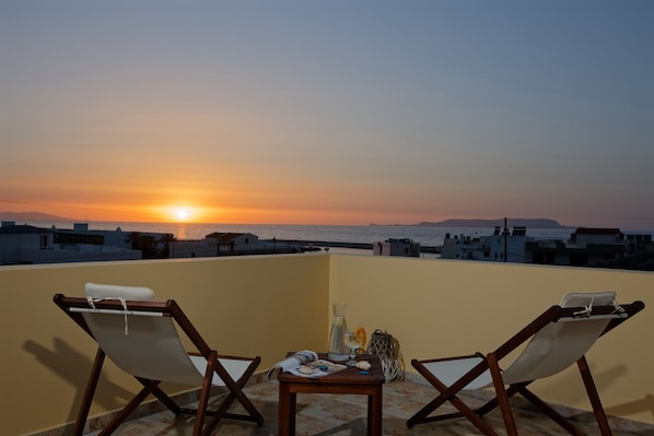 A terrace with two wooden chairs, a small table, and a view of the sunset over the sea. - Beatiful Villa in Gouves, Sea Views, Crete (Hersonissos)