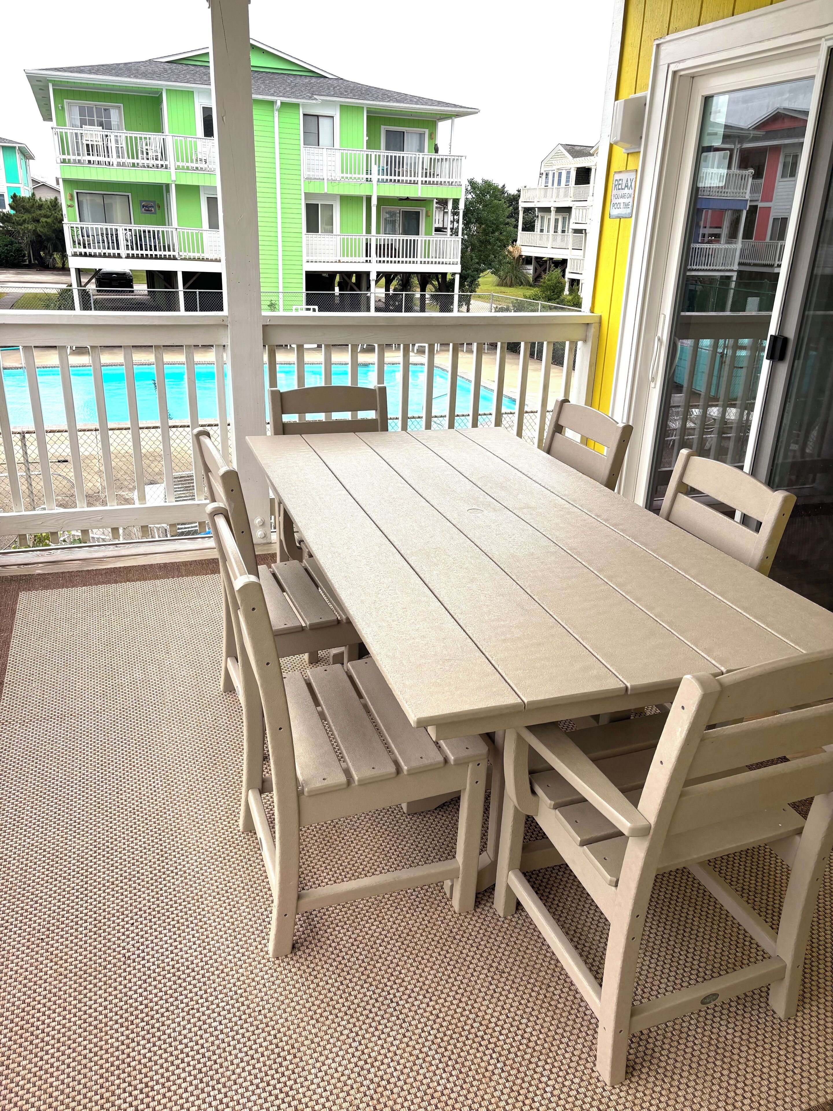 Un espacio al aire libre techado con mesa y bancos, con vistas a una piscina y edificios cercanos.