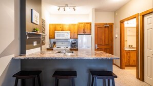 A kitchen with granite countertops, wooden cabinets, a microwave, stove, and refrigerator. There are three bar stools and a small island. - Ski in, Ski out Fireside Retreat  (Sun Peaks)