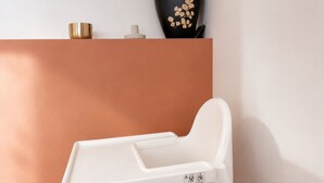 Ein weißer Babyhochstuhl mit Ablage, vor einer Wand mit braunem Unterteil und weißem Oberteil platziert.