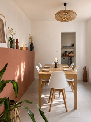 A dining area with a wooden table, white chairs, a candle, and a hanging light fixture. - The hacienda - Patio Terrace - Center / Beach 5 min (Le Havre)