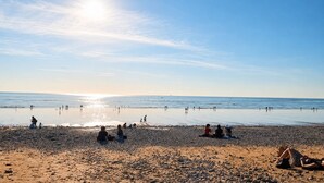 Ein Strand mit Menschen, die am Sand entlanggehen und darauf sitzen, und die Sonne ist am Himmel sichtbar.