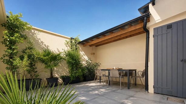 Eine Terrasse mit Tisch und Stühlen, umgeben von Topfpflanzen und einem grauen Tor.