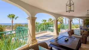 A spacious balcony with a view of the ocean, furnished with a sofa, a coffee table, and a hanging light fixture. - Palatial Villa in Hacienda Las Chapas, Marbella (Marbella)