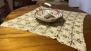 Un comedor con una mesa de madera, un plato decorativo y un camino de mesa de encaje.