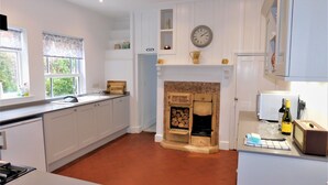 A modern kitchen with white cabinetry, a brick floor, a fireplace, and a clock on the wall. - Clarendon -  a house that sleeps 10 guests  in 5 bedrooms (Sheringham)