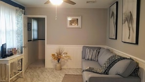 Un soggiorno con un divano grigio, un tavolino, una ventola a soffitto e un quadro appeso al muro.