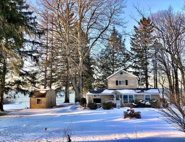 A two-story house with a snow-covered driveway and surrounding trees.