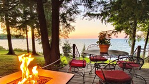 A deck with a fire pit, outdoor seating, and a view of the lake. - Pine Cottage - Beautiful direct lakefront cottage located in Sodus, NY, with full amenities. (Sodus)