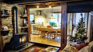 A cozy living room with a fireplace, a dining area, and a kitchen visible through an open door. - Pine Cottage - Beautiful direct lakefront cottage located in Sodus, NY, with full amenities. (Sodus)
