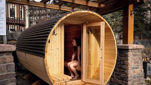 Una sauna in legno con ingresso curvo, una panca all'interno e una base in pietra.