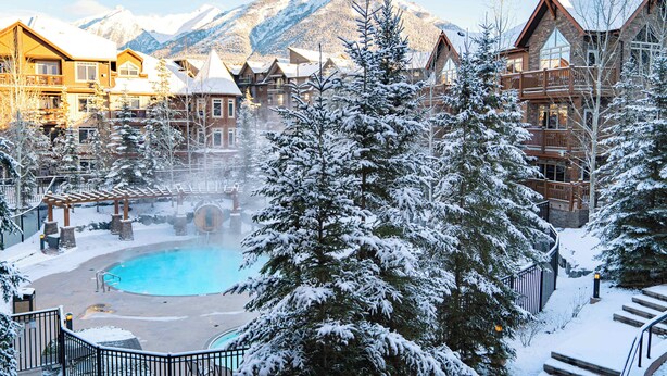 Un resort con piscina, alberi ricoperti di neve e vista sulle montagne.