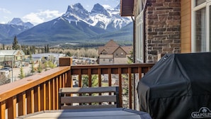 Un balcone con vista su montagne innevate, una ringhiera in legno e un barbecue coperto.