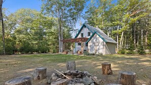 A rustic cabin with a wooden deck and a fire pit surrounded by tree stumps. - Brand new year round house with easy access to to everywhere in Ogunquit (Ogunquit)