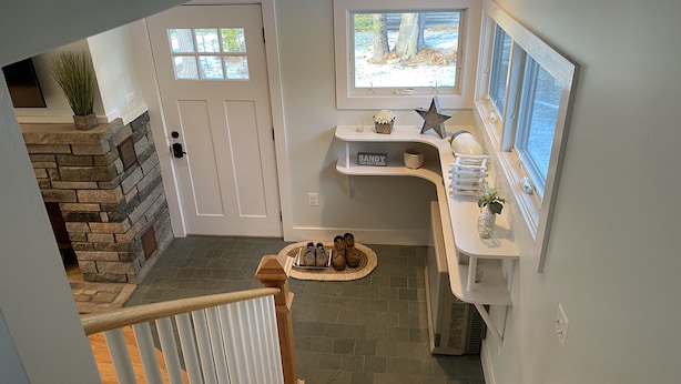 A modern interior with a stone fireplace, a wooden staircase, a kitchen area with a window view, and a small rug with shoes. - Brand new year round house with easy access to to everywhere in Ogunquit (Ogunquit)
