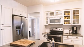 Une cuisine moderne avec des meubles blancs, des appareils en acier inoxydable et une planche à découper en bois posée sur le plan de travail.