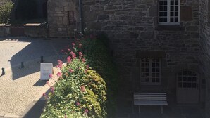 A stone building with a sloped roof and multiple windows, surrounded by cobblestone pavement and a flower bed. - Waterfront duplex in the heart of the historic center (Roscoff)