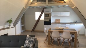 An attic bedroom with a bunk bed, a dining area with a table and chairs, a kitchenette, and a potted plant. - Waterfront duplex in the heart of the historic center (Roscoff)
