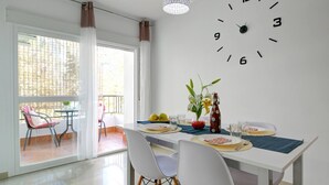 A dining area with a white table, chairs, and a wall clock. - Apartamento Palmeras 29 by Solset (Nerja)