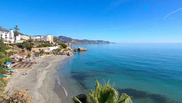 A coastal town with a sandy beach, clear blue sea, and buildings along the shore. - Apartamento Palmeras 29 by Solset (Nerja)