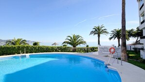 A clear blue swimming pool with a white deck, surrounded by palm trees and a view of the sea. - Apartamento Palmeras 29 by Solset (Nerja)