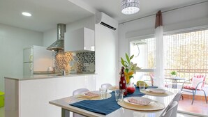 A modern kitchen with a central island, a dining area with a table set for four, and a view of the outdoors through large windows. - Apartamento Palmeras 29 by Solset (Nerja)