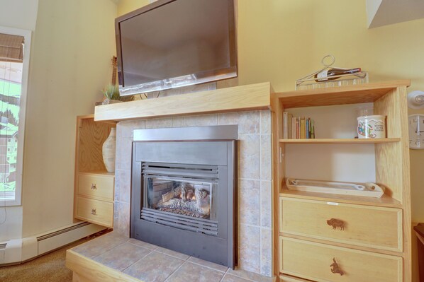 Ein Wohnzimmer mit Kamin, einem an der Wand befestigten Fernseher und Holzregalen mit Büchern und Dekoartikeln.