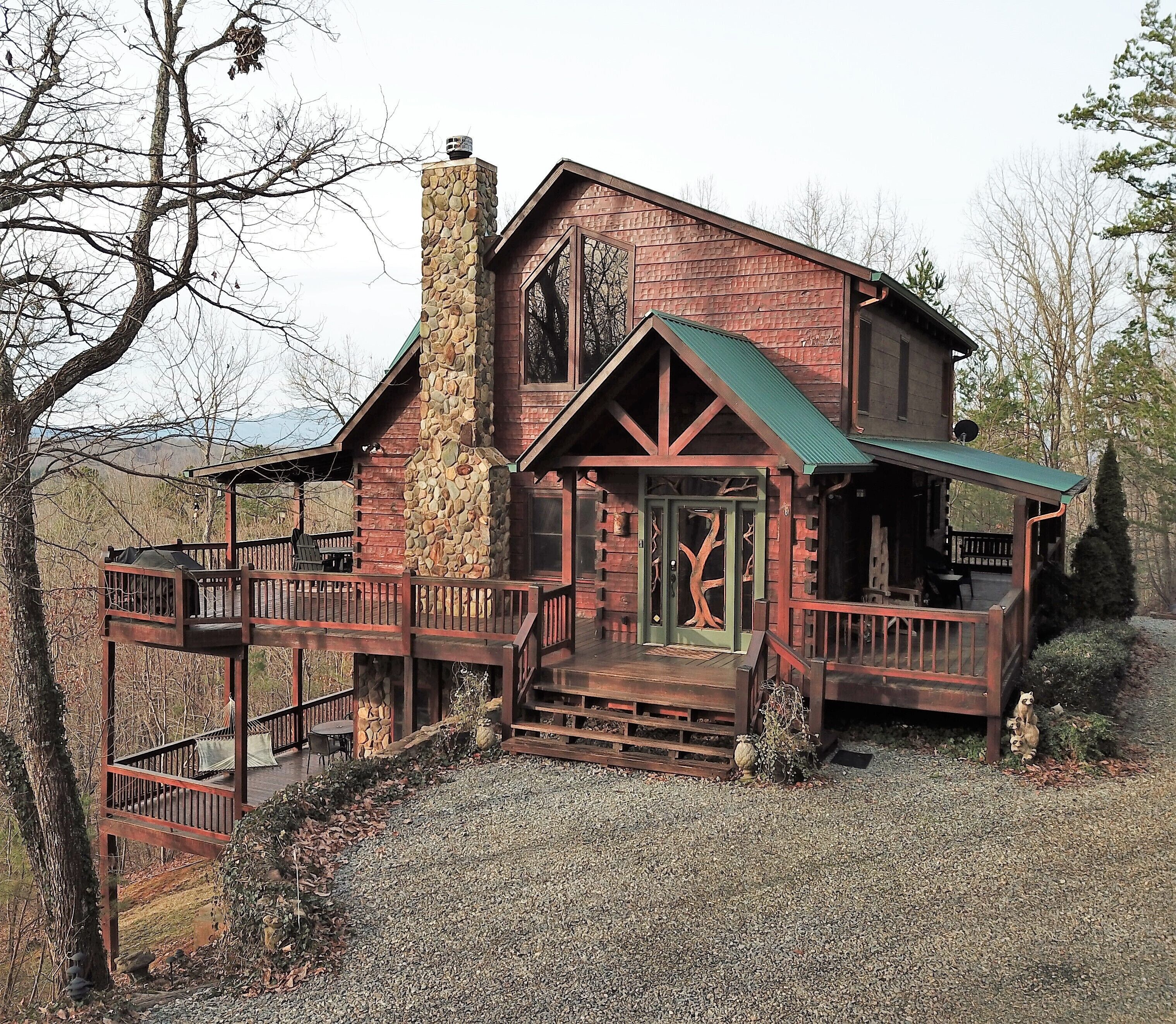 A rustic cabin with a stone chimney, a wooden deck, and a large window.