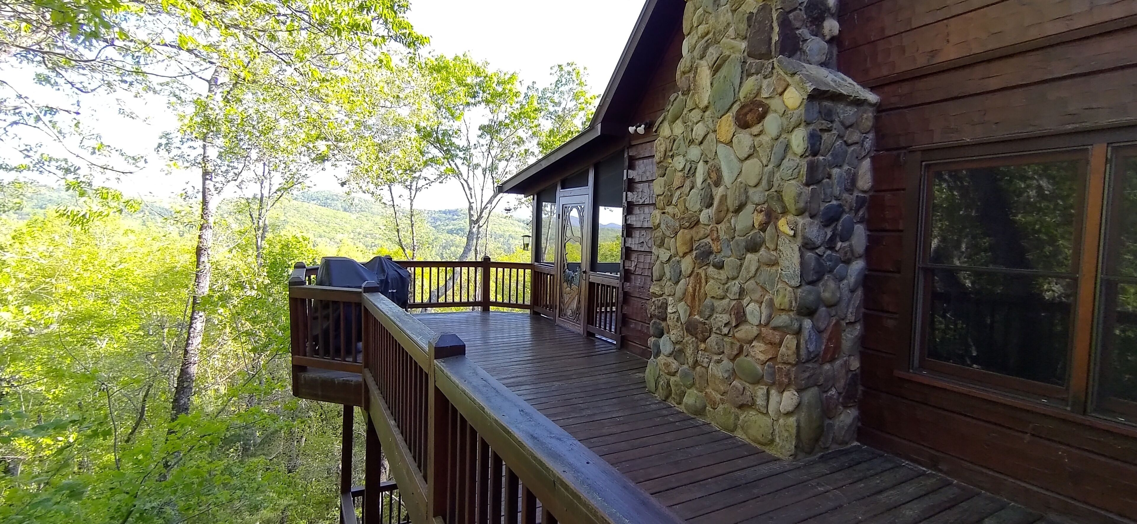 A wooden deck with a stone wall, overlooking a forested area.