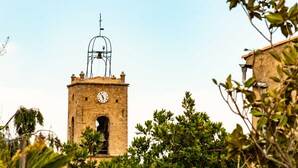 Una torre de piedra con un reloj, rodeada de vegetación.