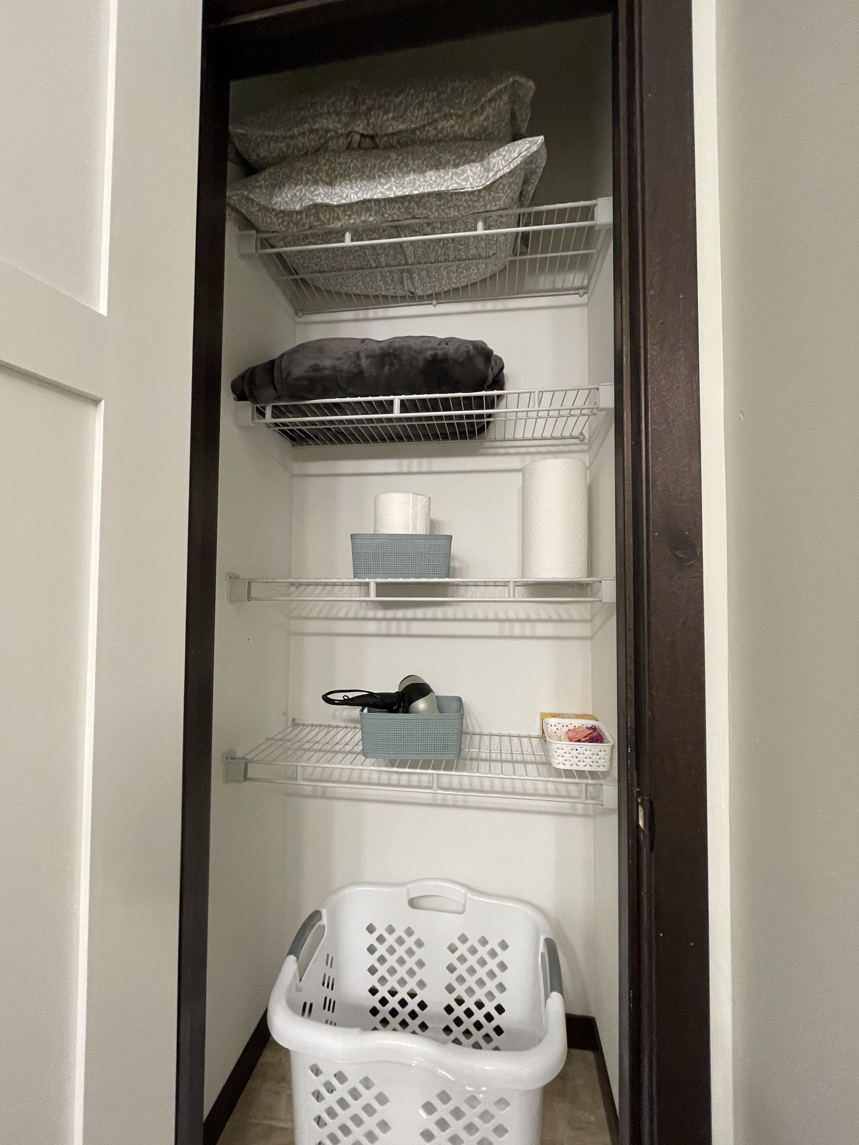 Un cuarto de lavado con repisas que contienen varios artículos, como una cesta, un almohón y un rollo de toallas de papel.