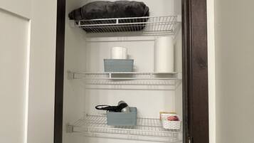 Un cuarto de lavado con repisas que contienen varios artículos, como una cesta, un almohón y un rollo de toallas de papel.
