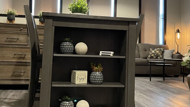 A modern living room with a dark wooden console table, shelves with decorative items, a grey sofa, and a dining area with a wooden chair and a cabinet. - NEW, NEW, NEW!  Wabasha downtown studio113 Pembroke Ave Unit #102 (Wabasha)