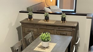 A dining area with a dark wooden table, chairs, and a bench. There are potted plants on the table and bench, and a small shelf with decorative items. - NEW, NEW, NEW!  Wabasha downtown studio113 Pembroke Ave Unit #102 (Wabasha)