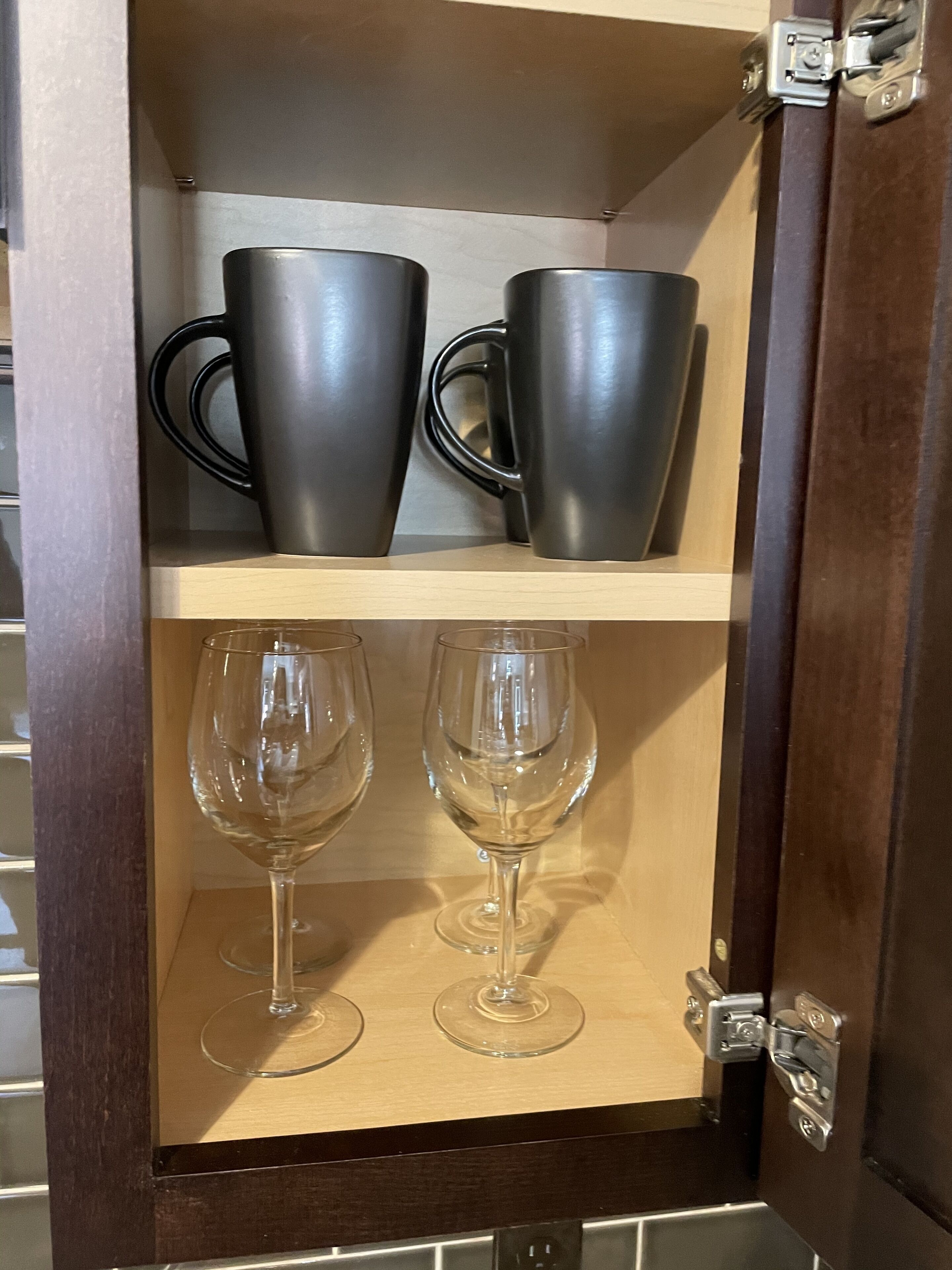 Un meuble en bois avec deux étagères. L’étagère supérieure contient deux tasses noires, et l’étagère inférieure contient deux verres à vin.