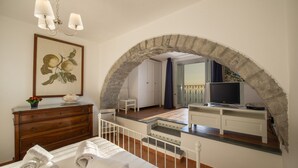 A bedroom with a stone archway, a wooden dresser, a bed with towels, a television, and a small table. - Villa Cimino - Central Villa Stunning Sea View (Praiano)