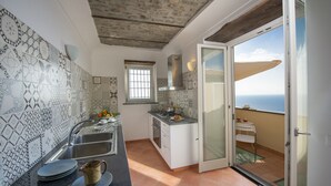 A kitchen with patterned tiles, a sink, and a view of the sea through a sliding door. - Villa Cimino - Central Villa Stunning Sea View (Praiano)