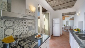 A modern kitchen with patterned tiles, a gas stove, and a dining area with a table and chairs. - Villa Cimino - Central Villa Stunning Sea View (Praiano)
