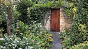 Un chemin de pierres menant à une porte en bois, entourée d’une végétation luxuriante et de plantes en fleurs.