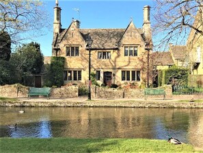 A historic stone building with a pond in front, benches, and a duck swimming.