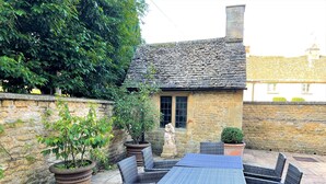 Une charmante maison en pierre avec un toit en tuiles, entourée de plantes en pot et de meubles en osier.